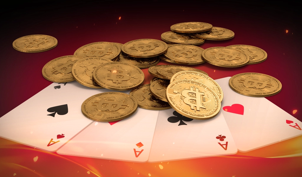 Lots of gold coins on a table with bitcoin logos on them. The coins are laying on top of four ace playing cards.